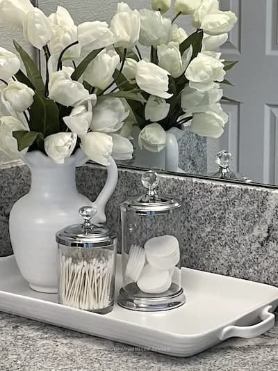 white flowers in a pitcher on a bathroom counter