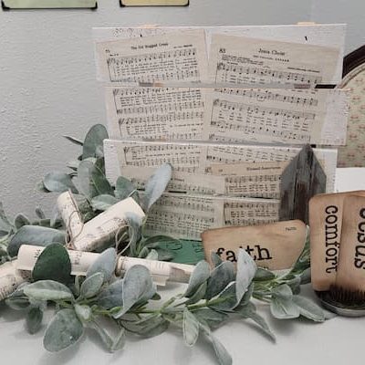 This wood pallet and old hymn art is a rustic farmhouse style decor piece that features sheet music from hymnals and a wooden chippy church.