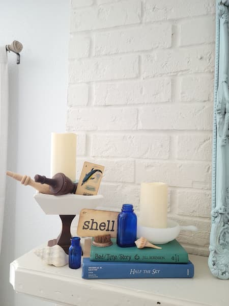 Fireplace mantel vignette with vintage books, seashells, pedestal candle holder and vintage flash cards