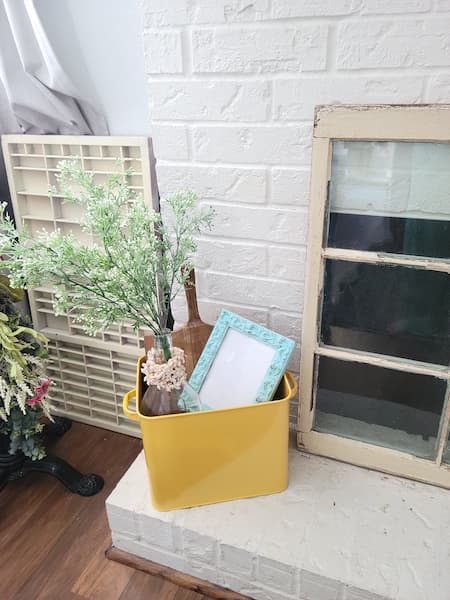 Fireplace hearth with yellow tin box - inside glass bottle with greenery, cutting board and frame