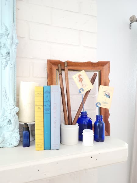 Fireplace mantel vignette with candle, vintage books, an empty frame, bottles with vintage flash cards