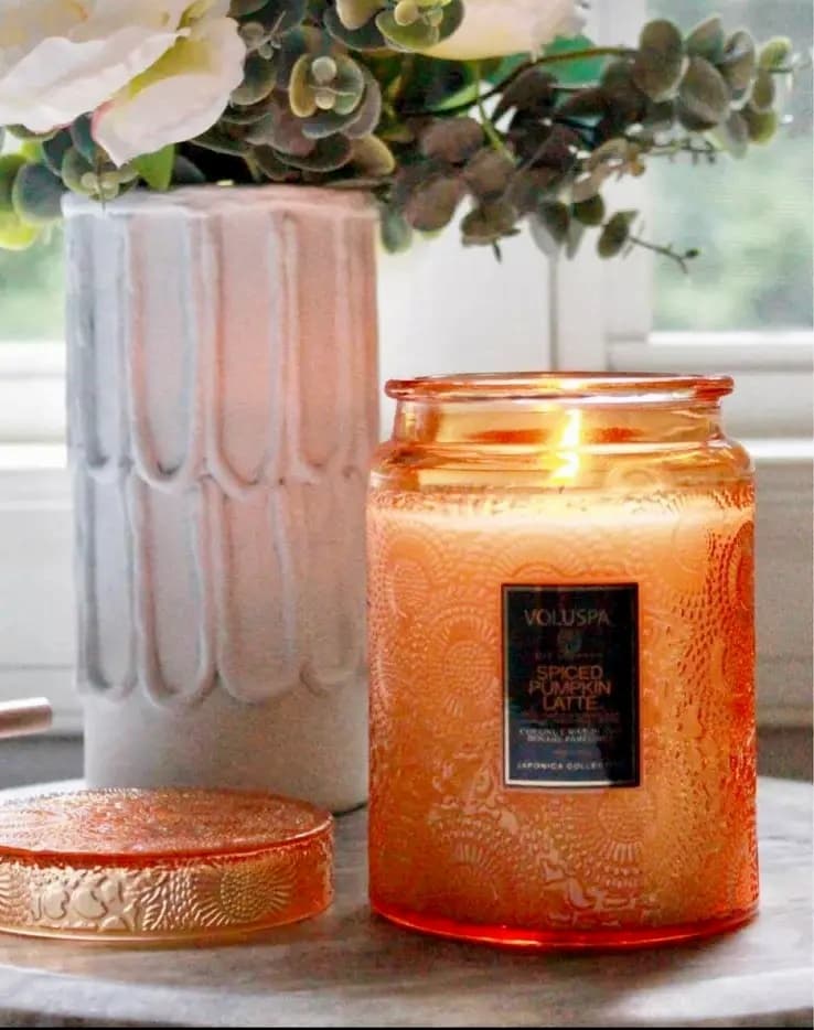 Lit Orange fall candle with white vase of flowers