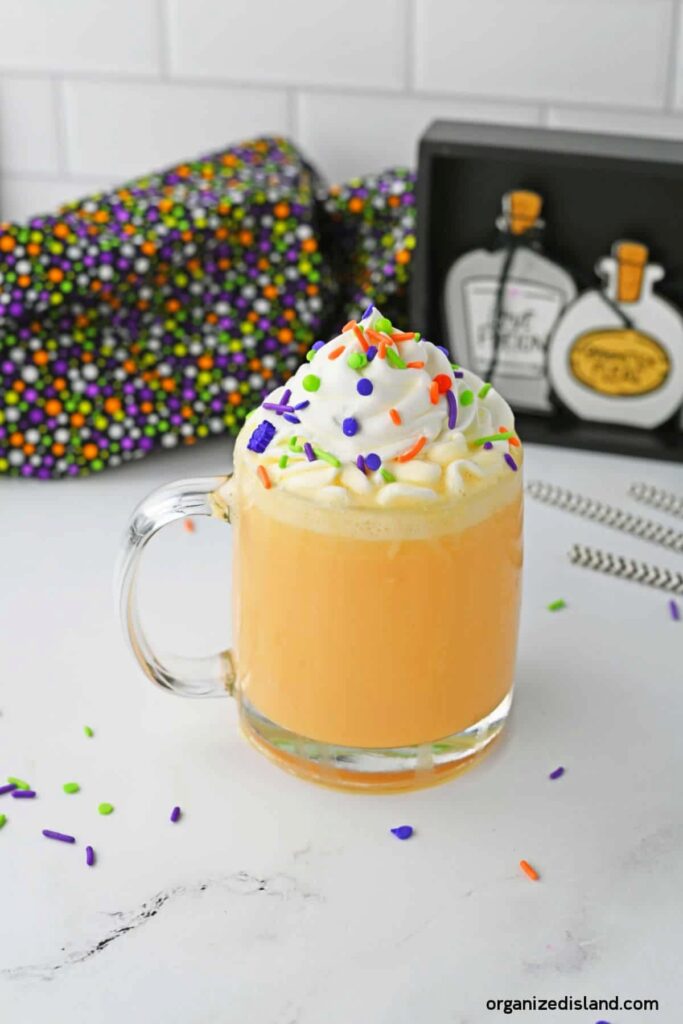 clear coffee mug with orange drink inside with whipped cream and sprinkles