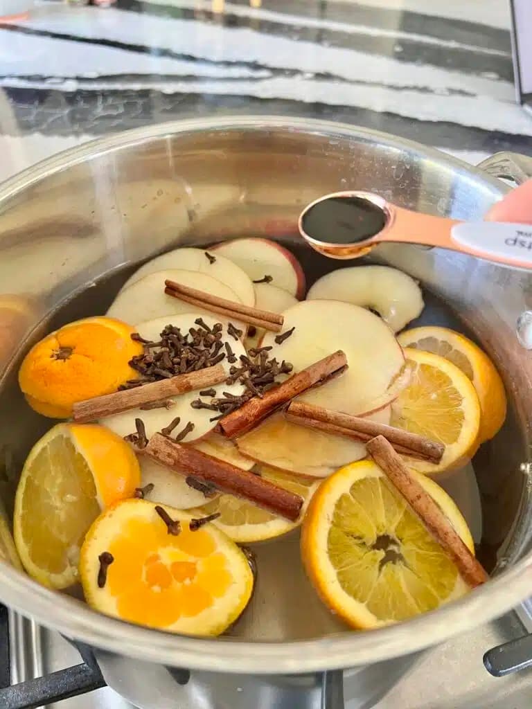 cinnamon sticks, apple and orange slices in silver pot of water