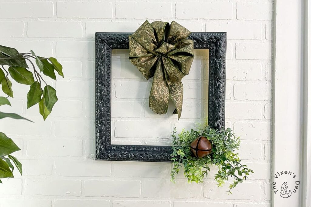 An empty black frame with bow and jingle bell with greenery