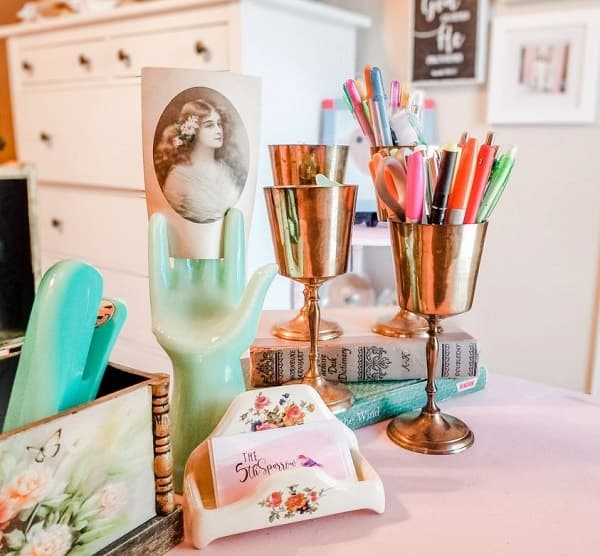 a pink desk with brass goblets for pens, a jadeite hand and a soapdish for business cards