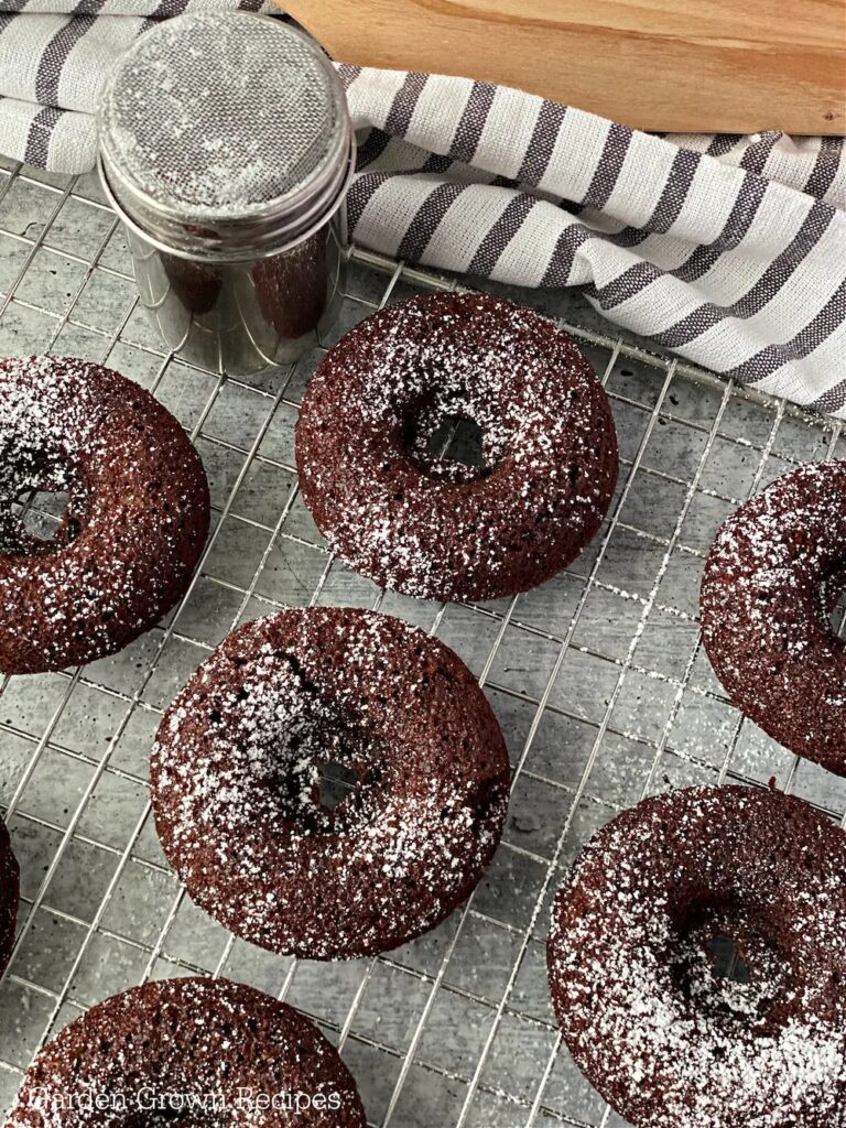 chocolate donuts with powdered sugar on cooling rack