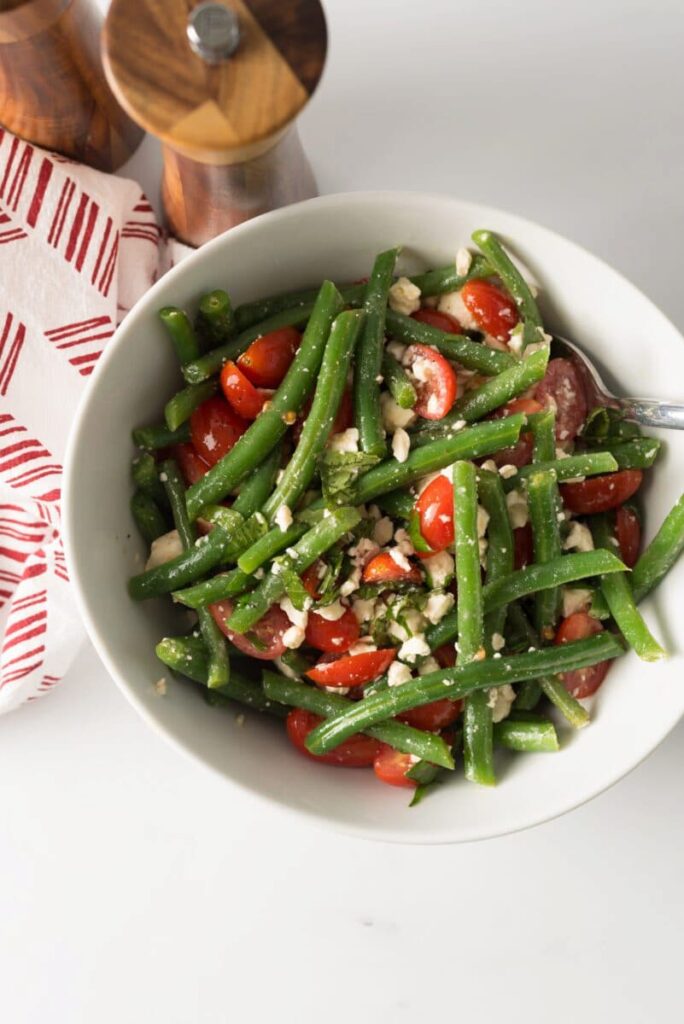 white bowl with green beans tomatoes and cheese