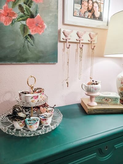 tiered tray of jewelry on green dresser and gallery wall